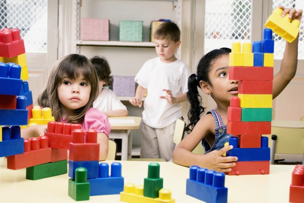 Two girls playing with plastic blocks with their friends in the background